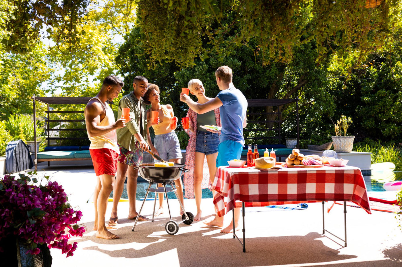 A group of friends stand around a barbecue during a backyard party.