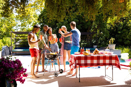 A group of friends stand around a barbecue during a backyard party.