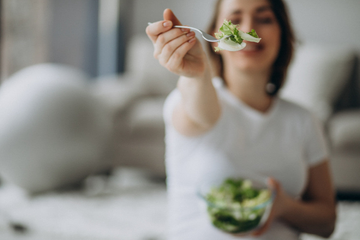 A female is reaching out her arm with a forkful of salad, while holding a glass bowl of green leafy salad with croutons. 