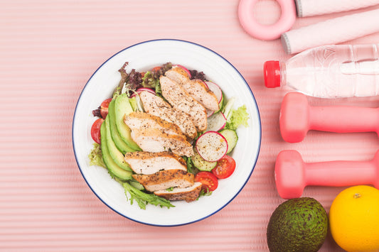 Fitness and active healthy lifestyles presentation concept with a plate of chicken breast salad, a lime, lemon, weights, and a bottle of water.